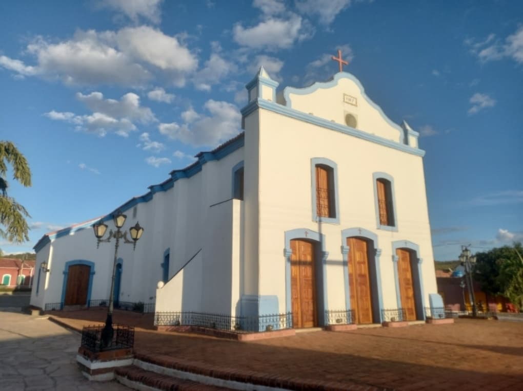 Fachada principal e vista lateral da Igreja do Senhor do Bonfim, com paredes brancas e detalhes em azul, no povoado de Caboclo.